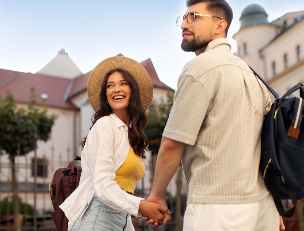 A couple holding hands looking behind them at a travel destination